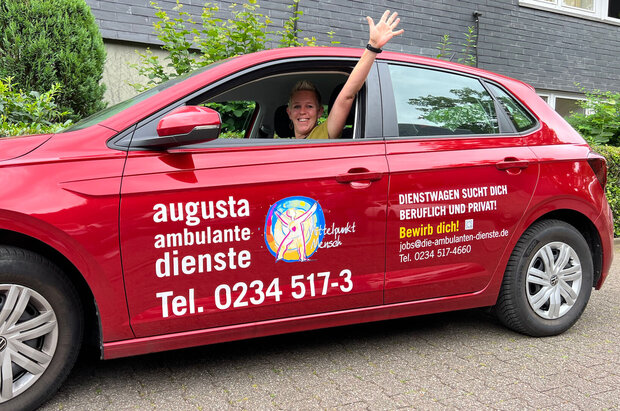 Mitarbeiterin winkt aus rotem Fahrzeug der Ambulanten Pflege